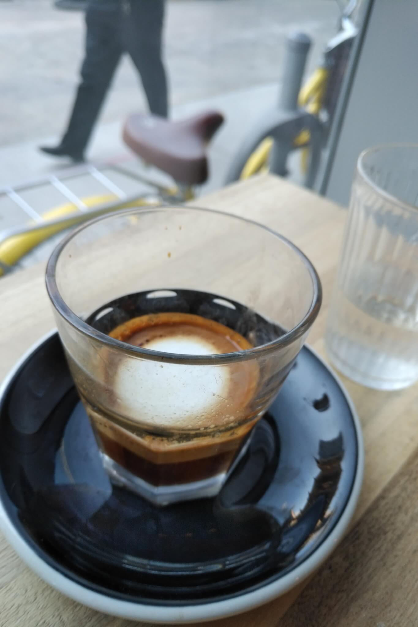 macchiato in a small glass. A bike leans against a post outside the window.