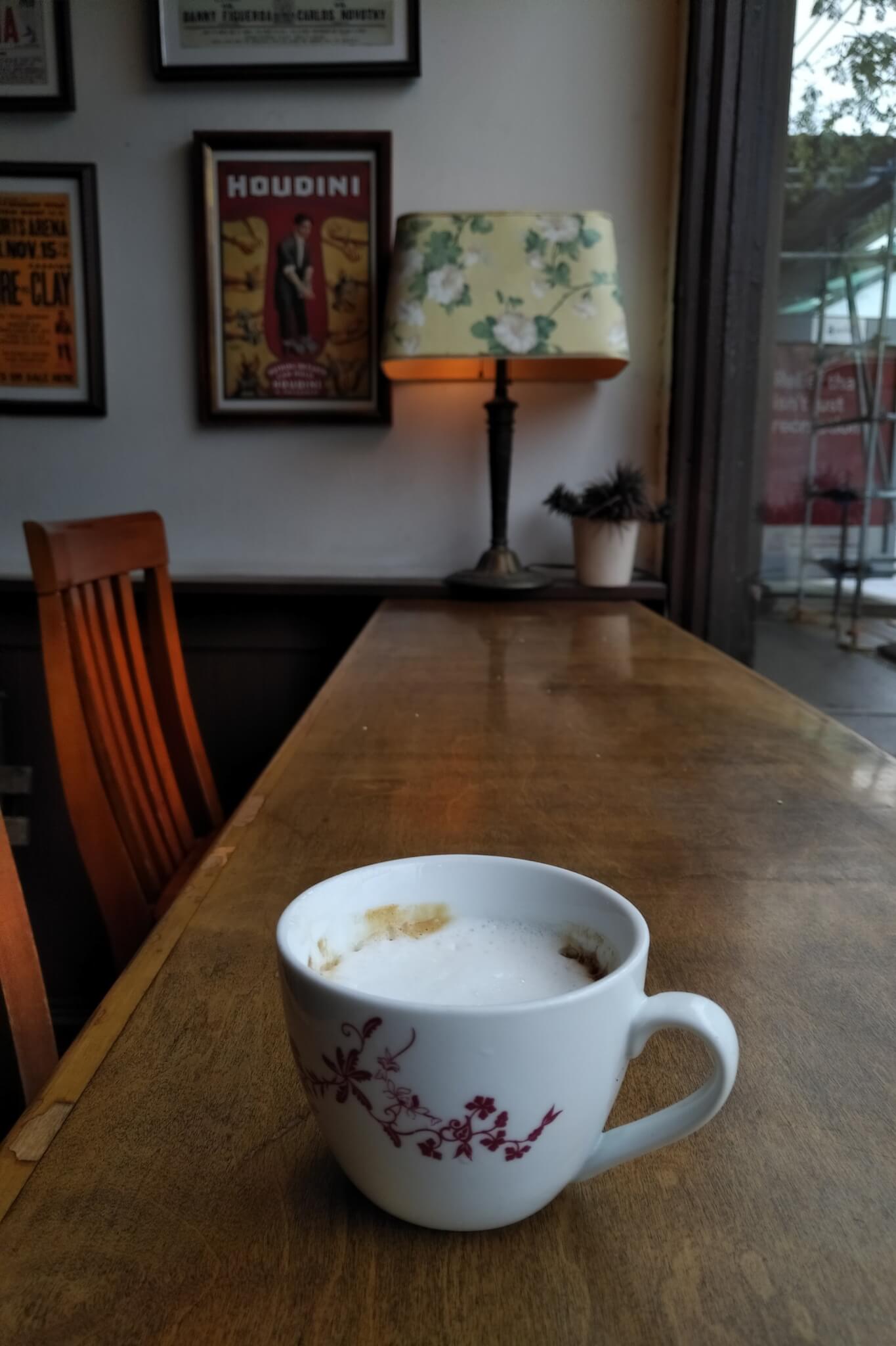 a macchiato on a long wooden counter with a table lamp at the far end in the background