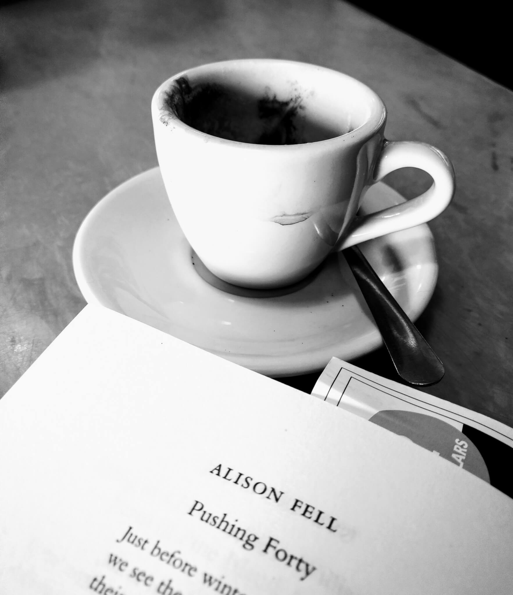 black and white image of an empty espresso cup with a poetry book open to a page titled "Pushing Forty"