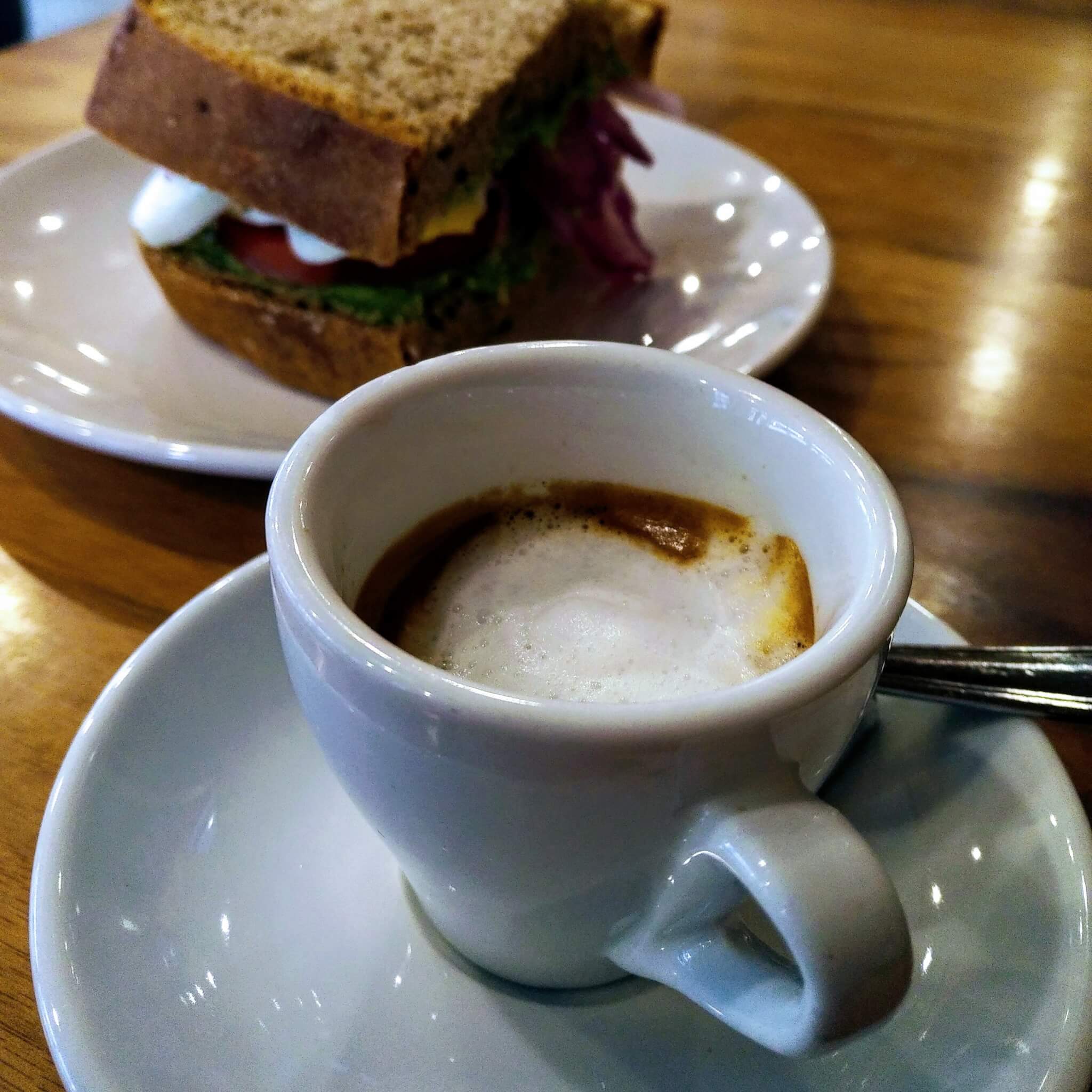 Macchiato with a sandwich sitting on a plate beside it
