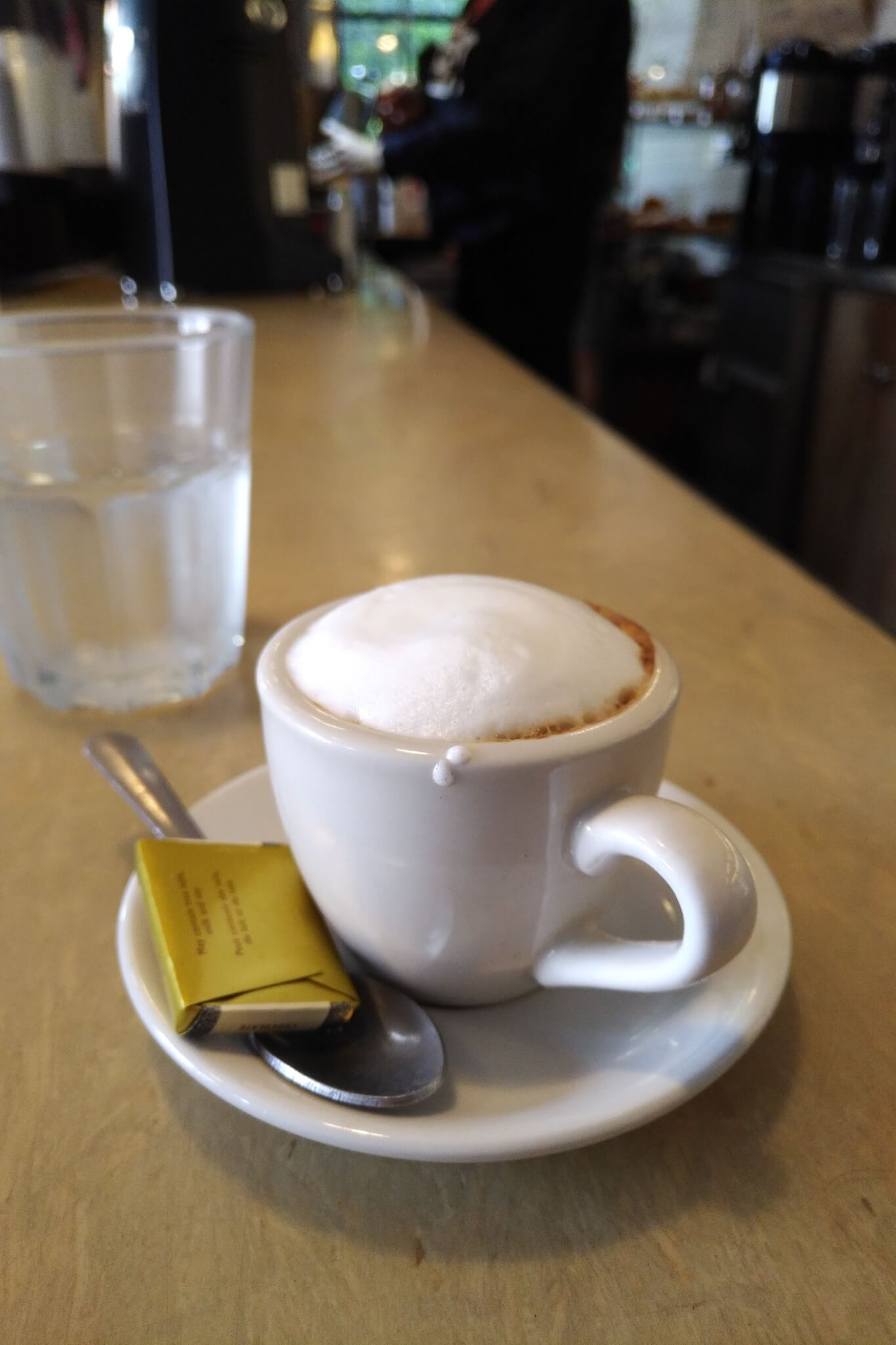 macchiato with a small foil-wrapped chocolate on the saucer