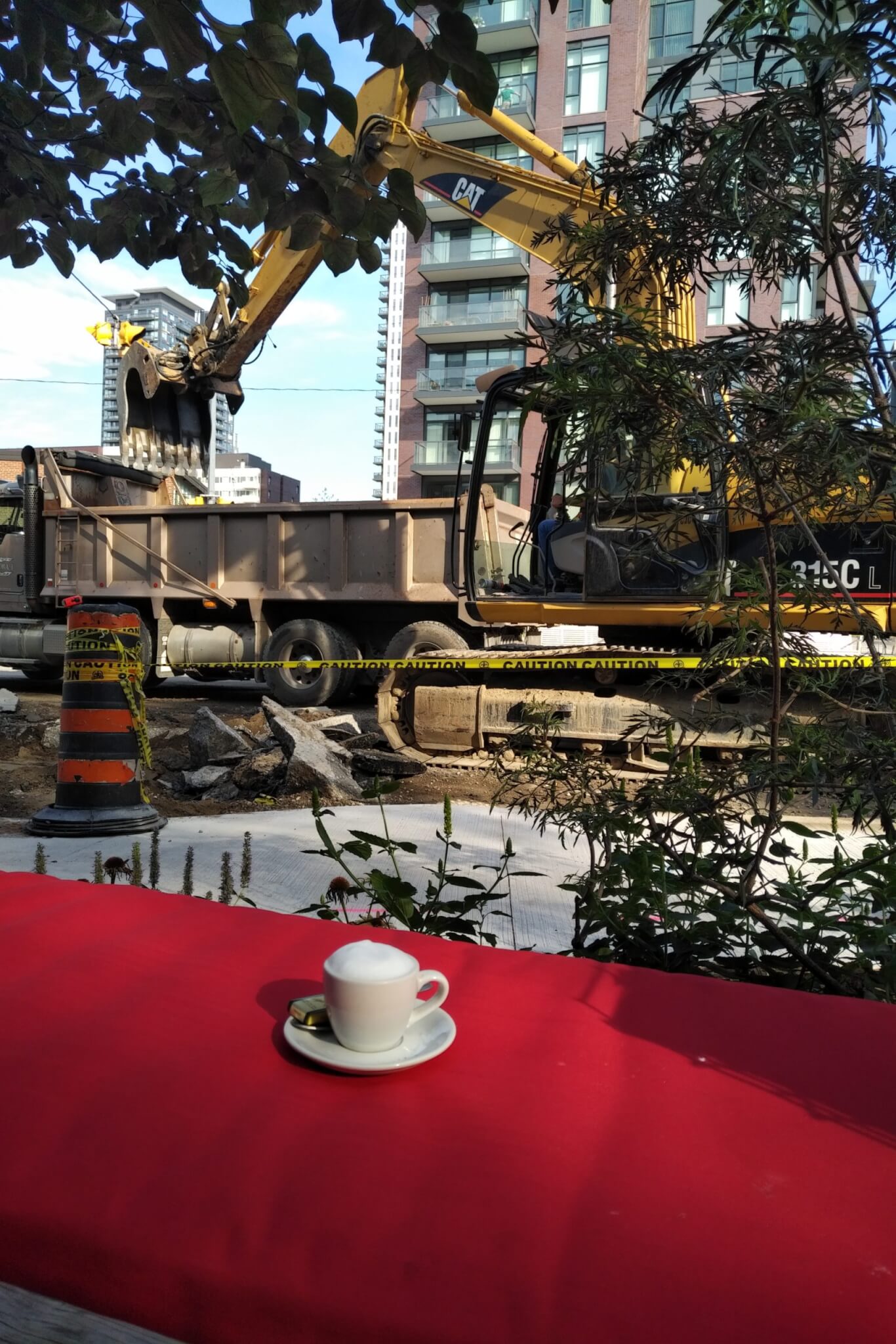 A small coffee on a bench in front of a backhoe digging up a road