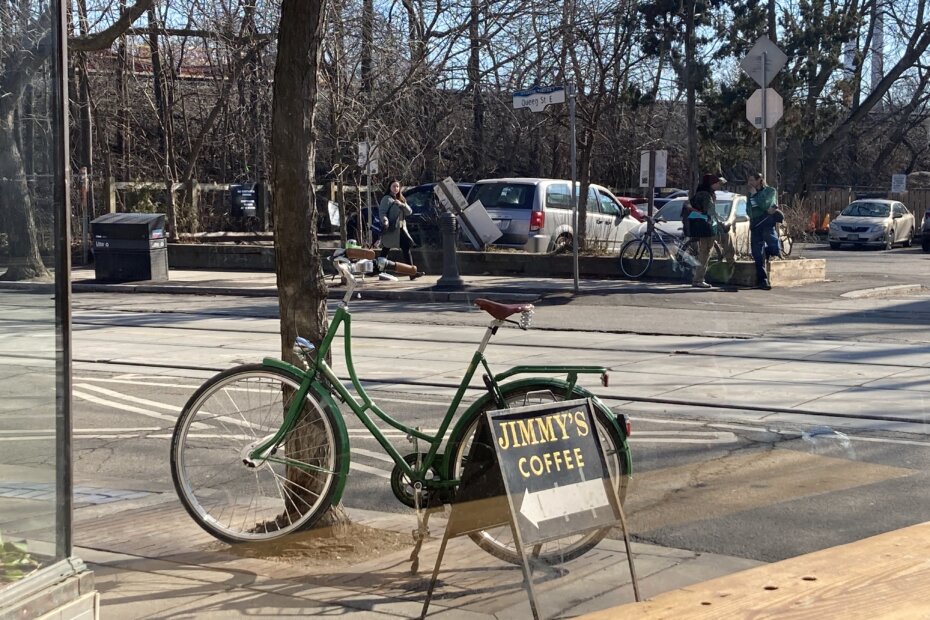 A green step-through bike parked beside a sandwich board which reads "Jimmy's Coffee"
